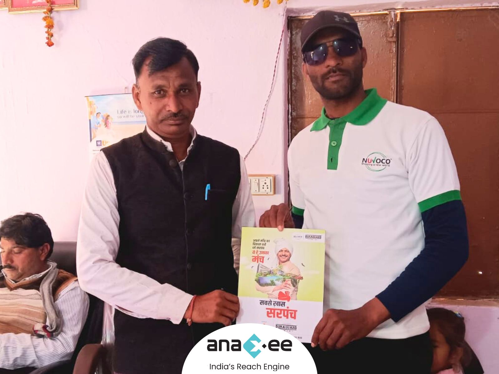 	“Anaxee Digital Runner presenting a ‘Sabse Khaas Sarpanch’ certificate and Nuvoco Duraguard Cement brochure to the village sarpanch inside a rural panchayat office.”
