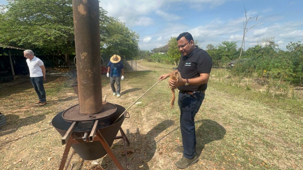 Person feeding agricultural residues into a pyrolysis unit for biochar production in an outdoor field setup.